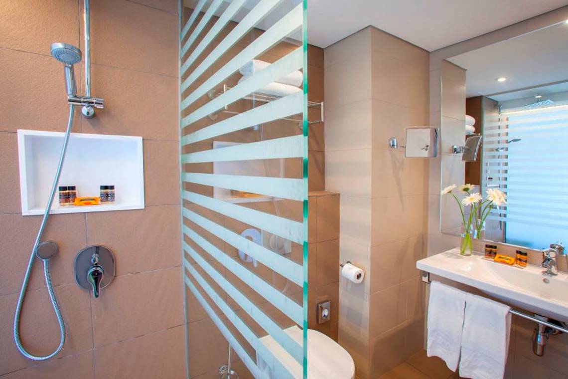 Badezimmer im Faros Hotel Ayia Napa mit Glasdusche, Toilette und Waschbecken.