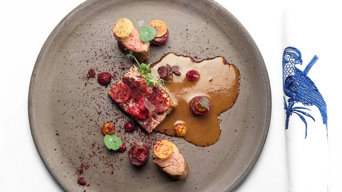 Ein Teller mit gebratenem Fleisch, Beilagen und roter Sauce, serviert auf einem grauen Teller.