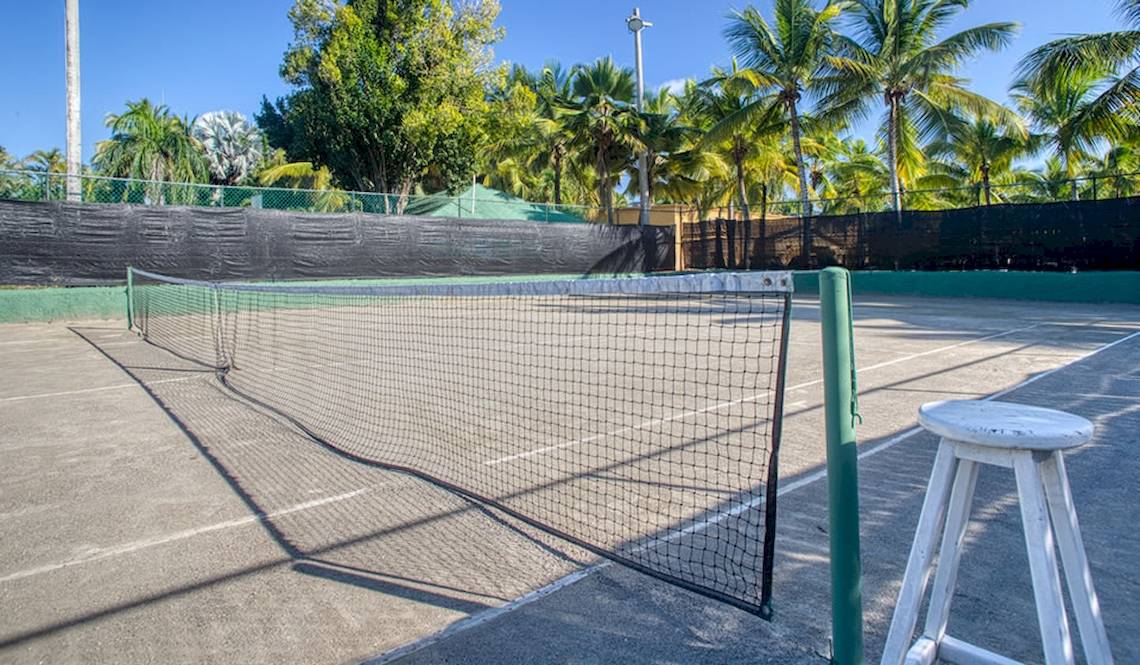 Tennisplatz im Coral Costa Caribe Strandresort mit Netz, Schatten und Palmen im Hintergrund
