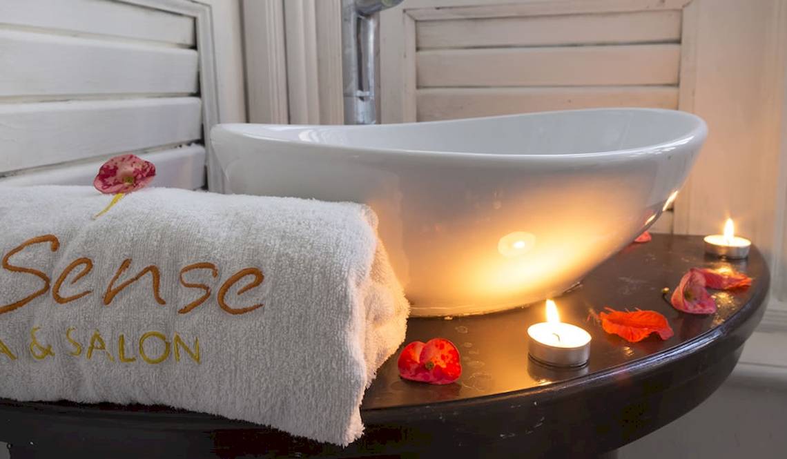 Ein Badezimmer im Coral Costa Caribe Beach Resort mit einem beleuchteten Waschbecken und einem Handtuch, das Sense & Salon beschriftet ist.