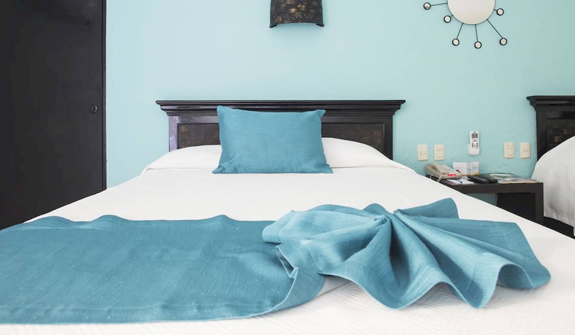 Bett im Hotelzimmer des Coral Costa Caribe Beach Resort mit blauer Bettwäsche und Kissen.