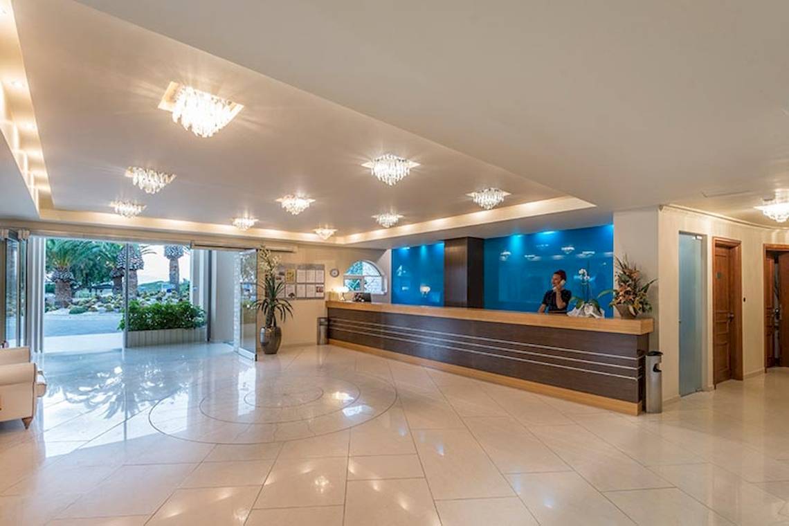 Rezeption des Sandy Beach Hotel in Kos mit einer Frau am Empfang und Pflanzen.