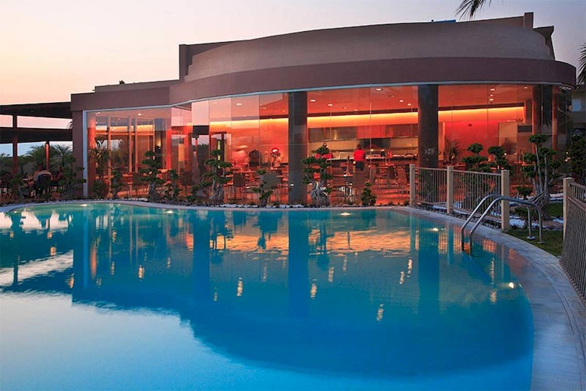 Abendlicher Außenbereich des Sandy Beach Hotels in Kos mit beleuchteter Bar und Pool.