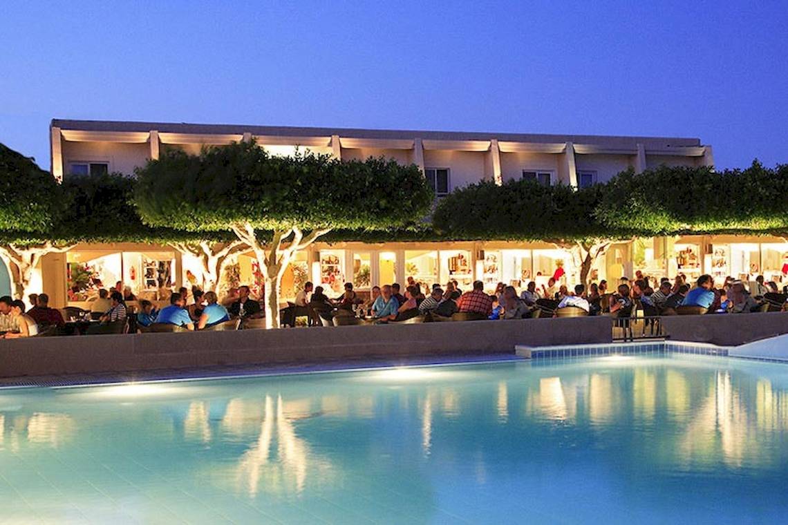 Abendliche Pool-Lounge im Sandy Beach Hotel auf Kos mit Gästen, die sich unter Bäumen versammelt haben.