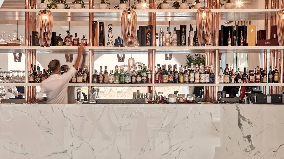Ein Barkeeper steht im Cocktailbereich der Katikies Villas Mykonos und serviert Getränke.