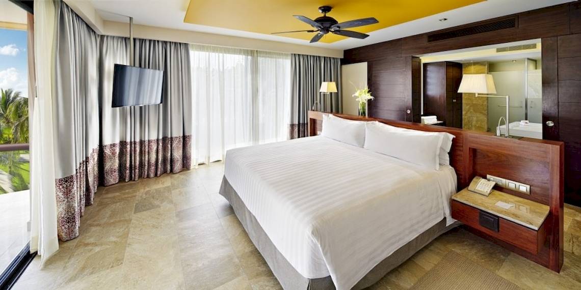 Hotelzimmer im Barcelo Maya Beach mit großem Bett, Fernseher und Fenstern.