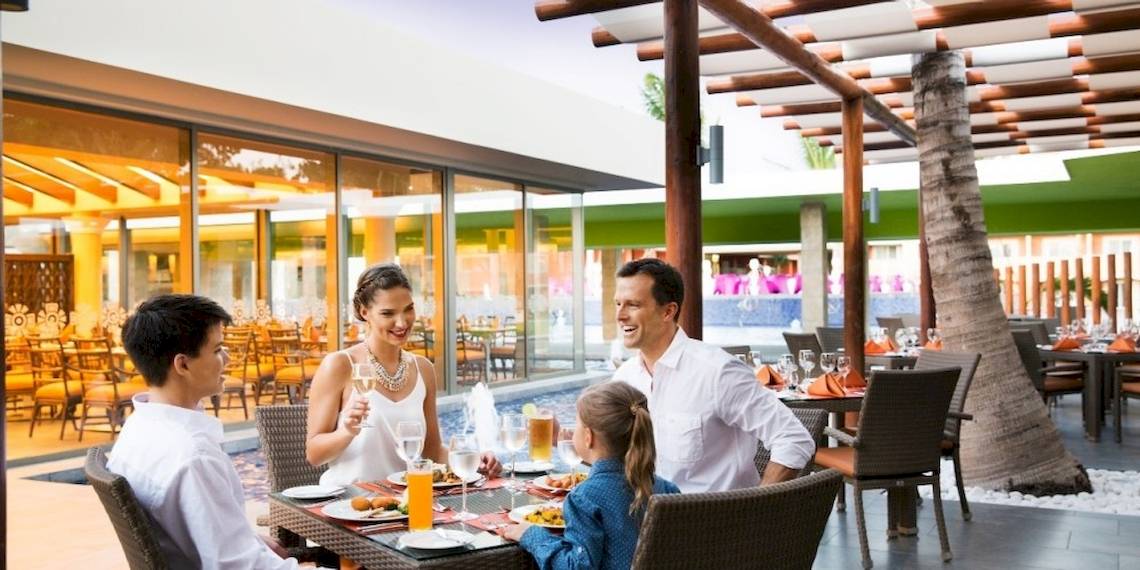 Familie sitzt am Tisch und genießt Essen im Barcelo Maya Beach Hotel Restaurant.