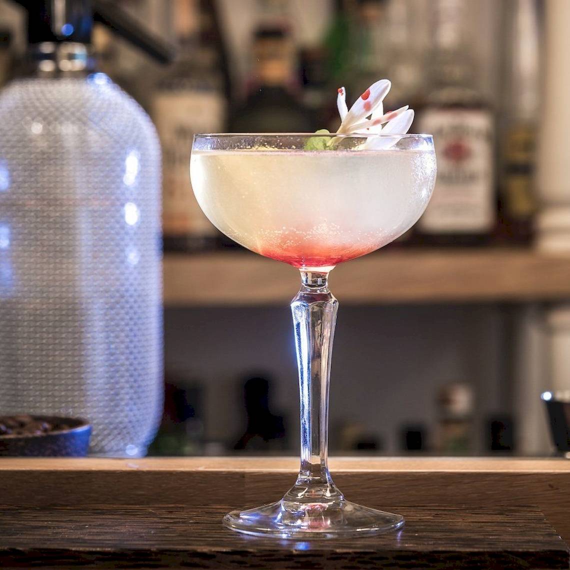 Ein Cocktail in einem Glas auf einer Bar mit einer Blume obenauf.