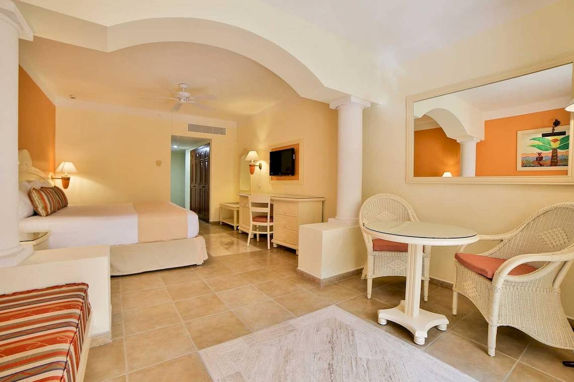 Hotelzimmer im Bahia Principe Grand Coba mit Bett, Schreibtisch, Spiegel und Korbstühlen.