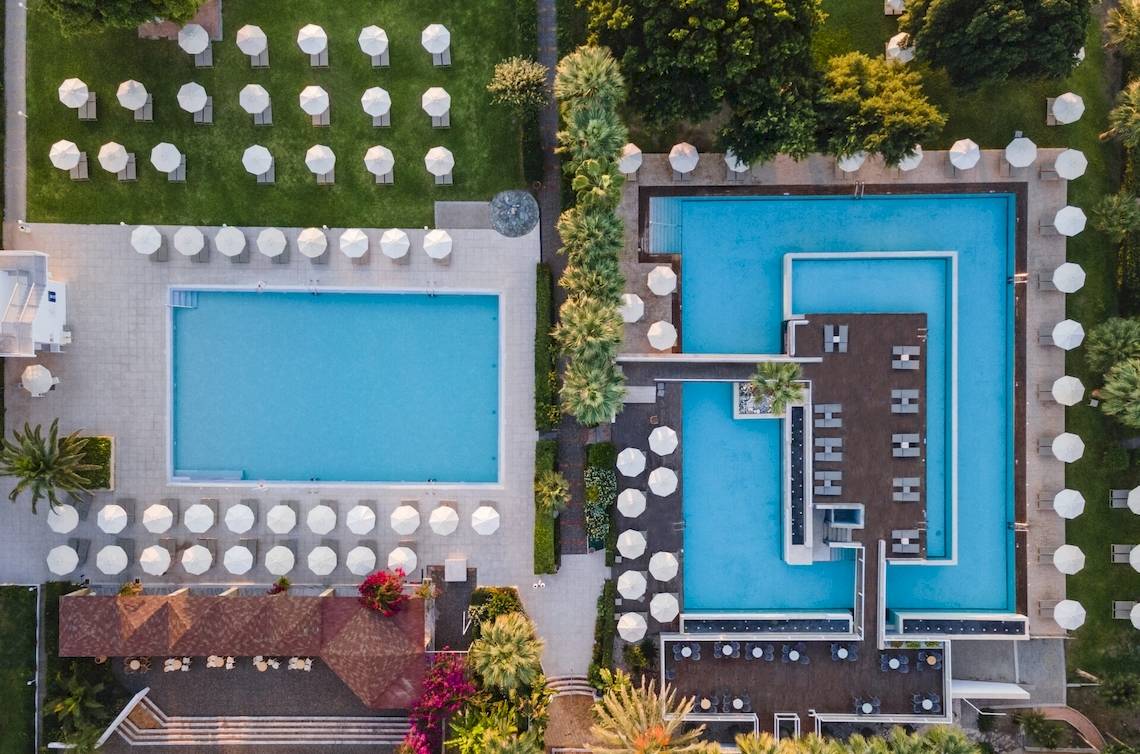 Luftaufnahme des Blue Sea Beach Resorts mit zwei Swimmingpools und vielen Sonnenschirmen.
