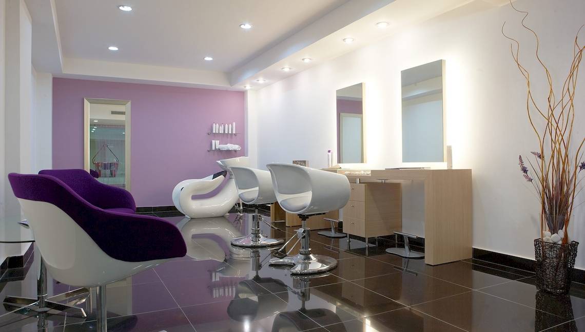 Friseursalon mit violetter Wand, weißen Stühlen und Spiegeln.
