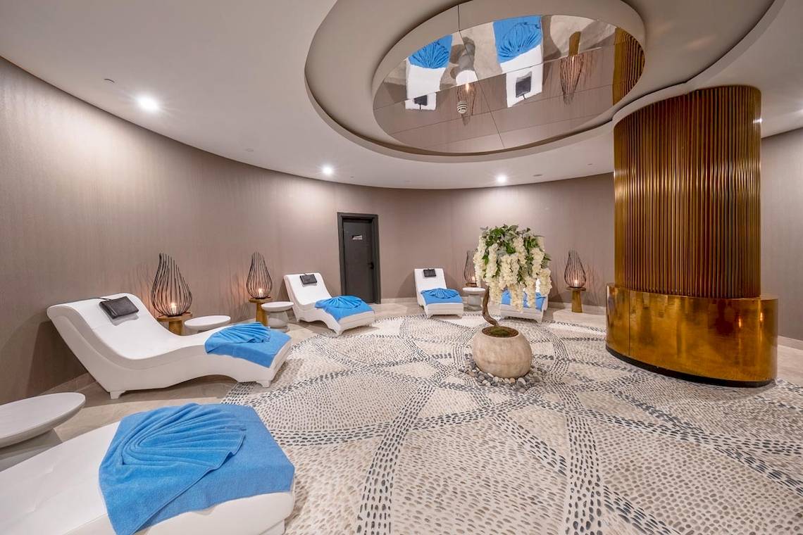Innenbereich des Spa-Bereichs des Lago Hotels mit weißen Liegen und blauen Handtüchern.