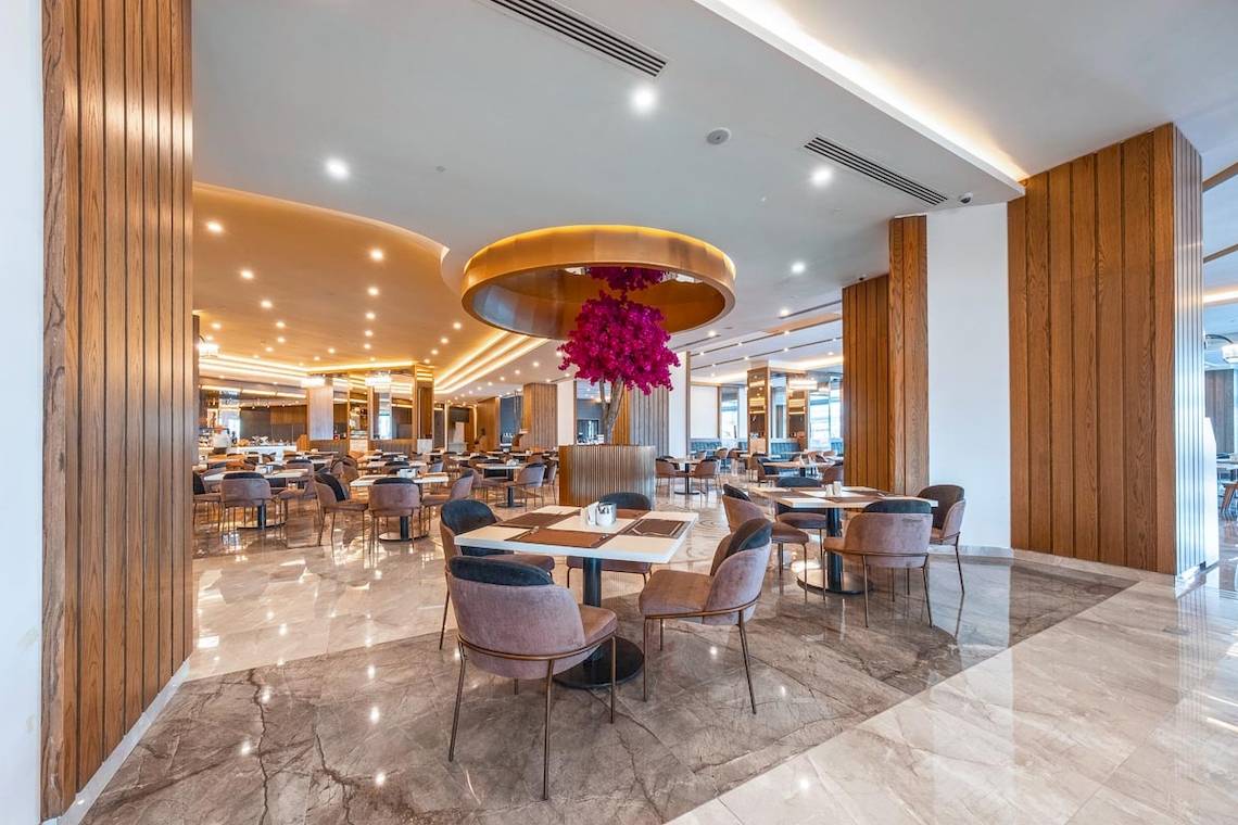 Innenbereich des Lago Hotels Restaurant mit Holzwänden und Marmorboden, vielen Tischen und Stühlen.