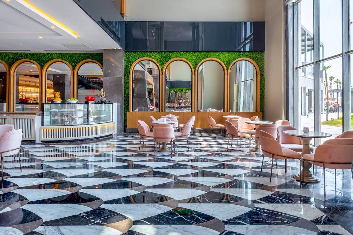 Innenbereich des Lago Hotels mit marmorierten Boden, pinken Stühlen und Tischen sowie grüner Wandverkleidung.