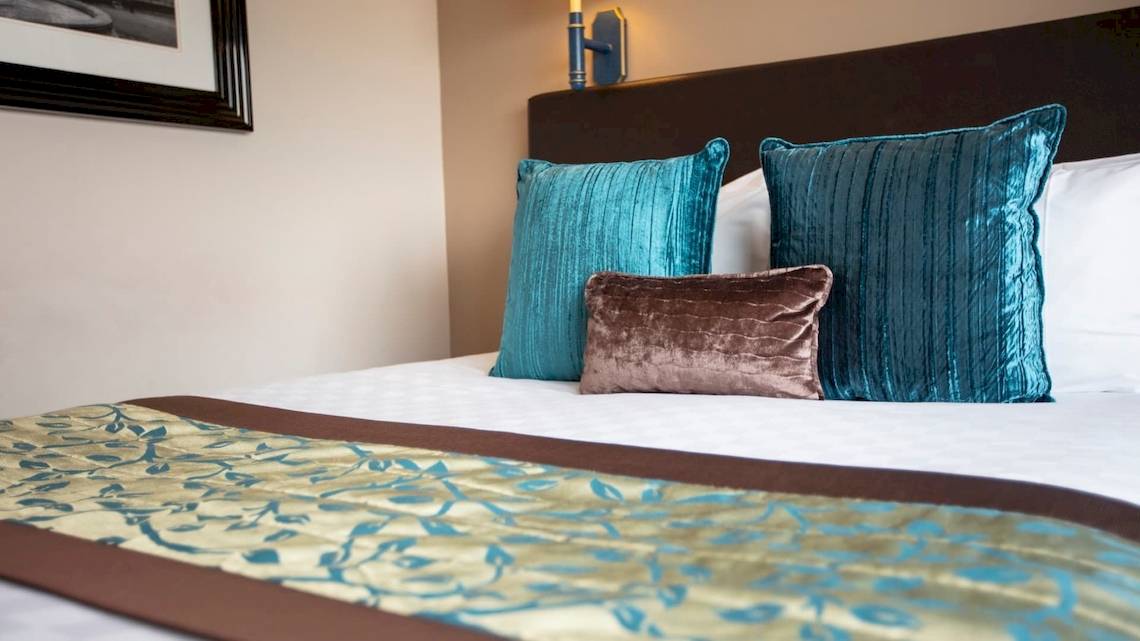 Das Bett im Tower Hotel London mit blauen und braunen Kissen und einer Wand dahinter.