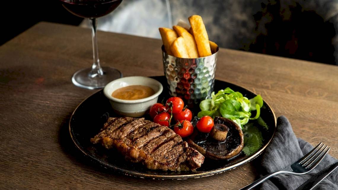 Ein Steak-Platter mit Beilagen und Salat auf einem schwarzen Teller im Tower Hotel, London.