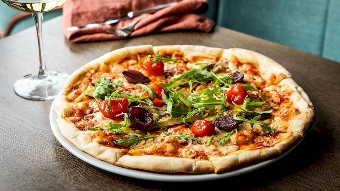 Eine Pizza mit Tomaten, Rucola und Oliven auf einem Holztisch im Tower Hotel, London.