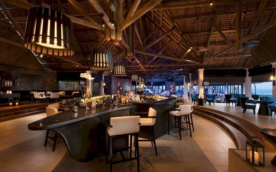 Innenansicht der Bar im Constance Ephelia Mahe Seychelles mit hohen Holzdecken und weißen Stühlen.