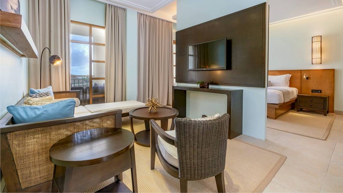 Innenansicht eines Hotelzimmers im Savoy Seychelles Resort & Spa mit Wohnzimmerbereich, Bett und Fernseher.