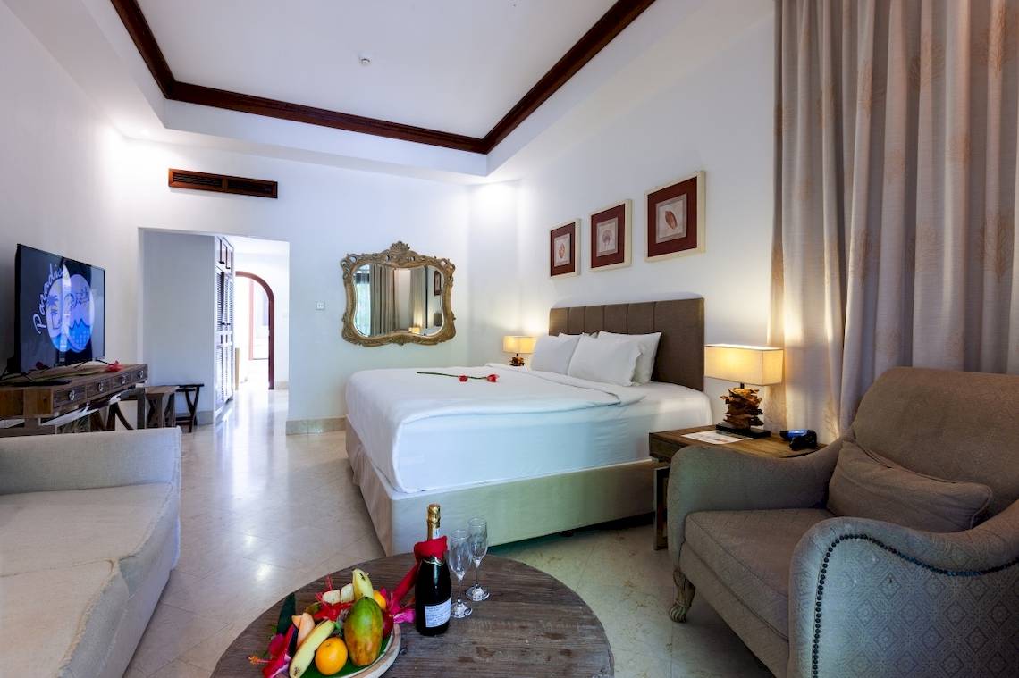 Hotelzimmer mit einem Bett, einer Lampe, einem Tisch mit Flasche und Gläsern, und Dekoration.