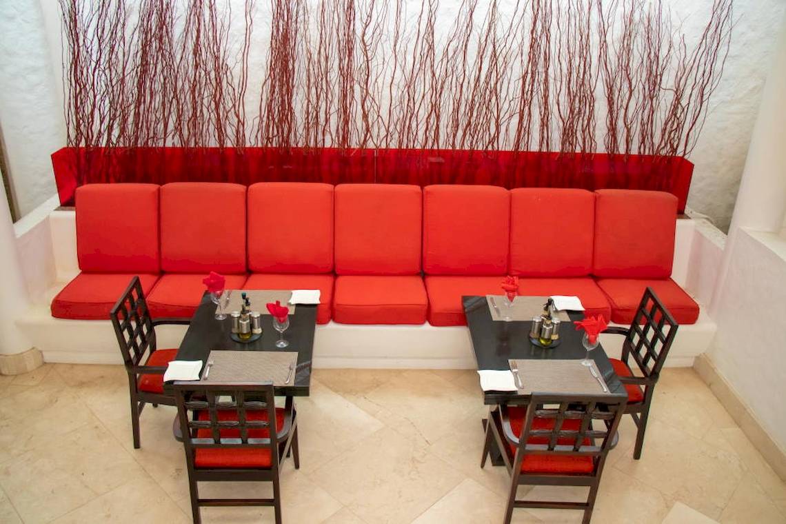 Roter Sofa im Restaurant mit zwei Tisch davor, roter Wand im Hintergrund.