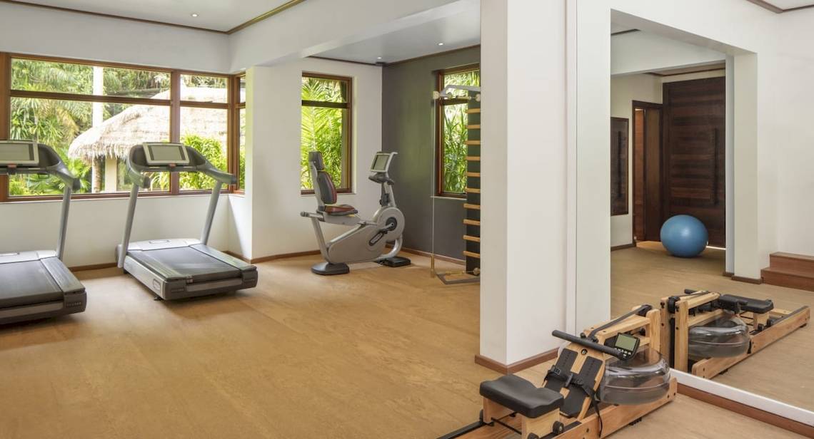 Fitnesszentrum im Anantara Maia Seychelles Villas mit Laufbändern, Rudergeräten und einer großen blauen Kugel.