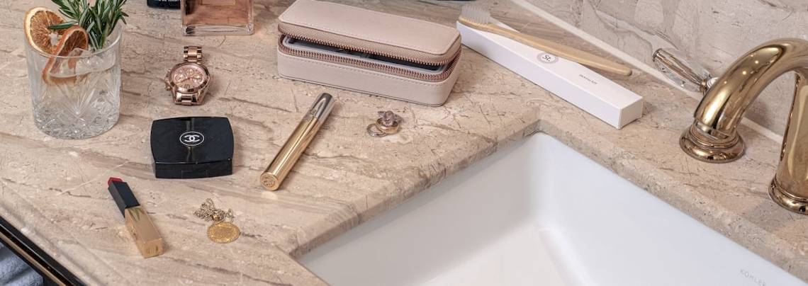 Badezimmer-Gegenstände im Saint Hotel, London, einschließlich einer Uhr, eines Parfüms, eines Glases mit Orangenscheibe, eines Kosmetiktäschchens, eines Zahnbürstenhalters, eines goldenen Zahnstochers, eines Kosmetikpinsels, eines Lippenstifts, eines Rings, einer Kette und eines Waschbeckens.