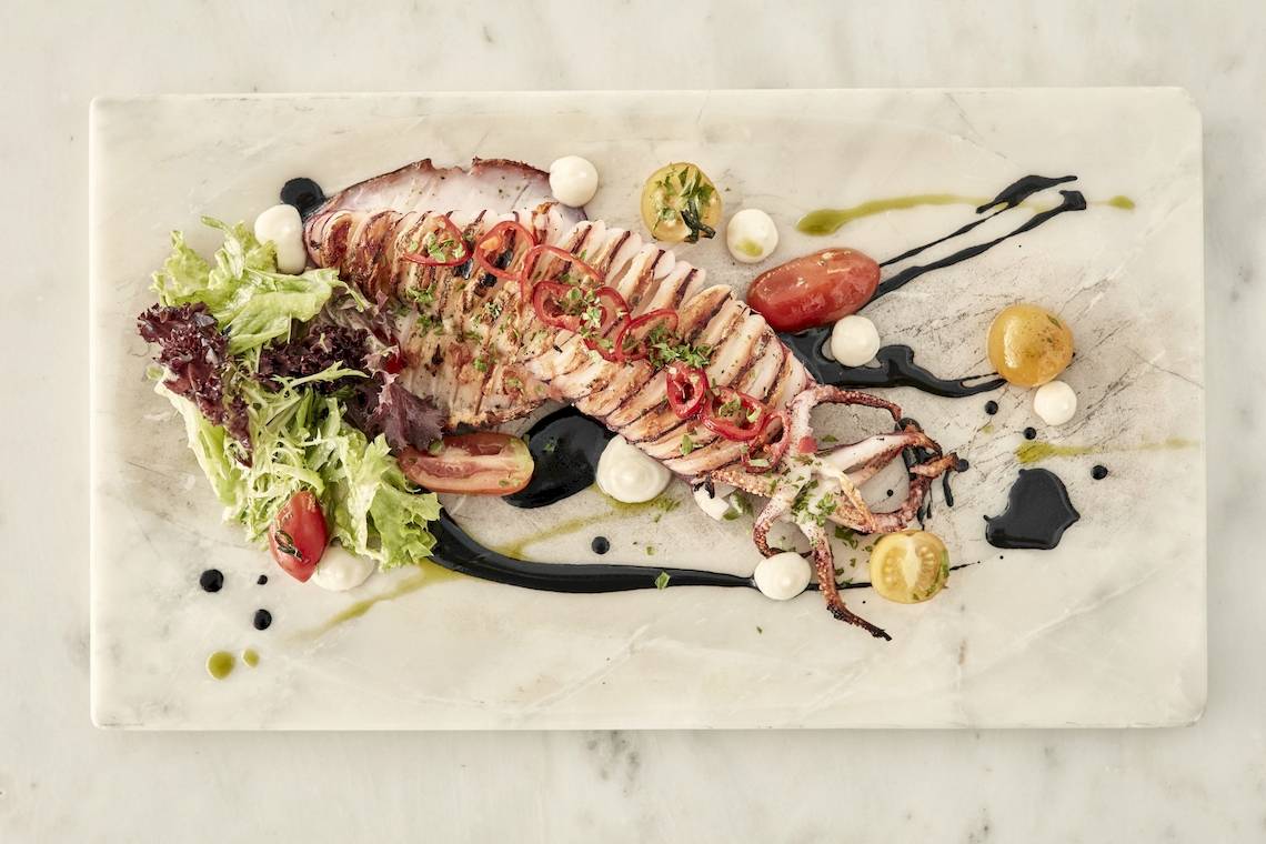 Gegrillter Tintenfisch mit Salat und Gemüse auf einem weißen Marmorteller.