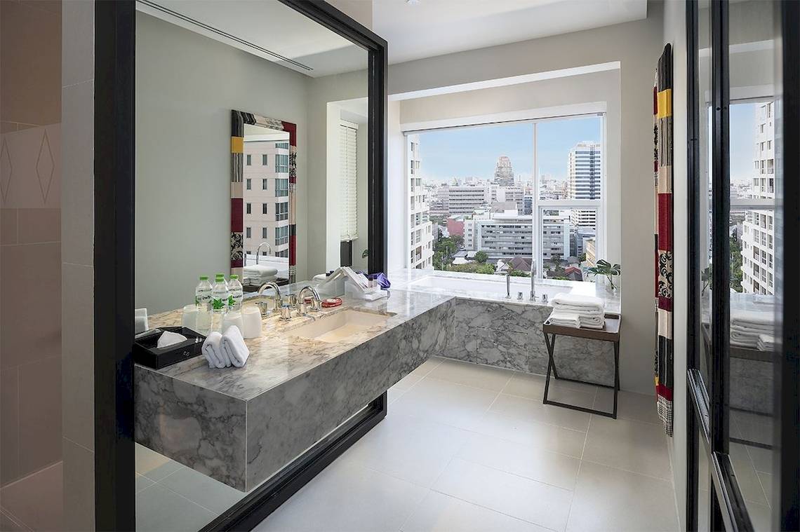 Ein Badezimmer im Mode Sathorn Hotel mit Marmorwaschtisch und Badewanne mit Blick auf die Stadt.