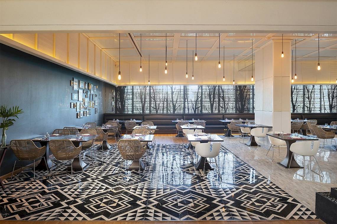 Innenansicht des Mode Sathorn Hotels Restaurants mit Tisch und Stühlen und hängenden Lampen.