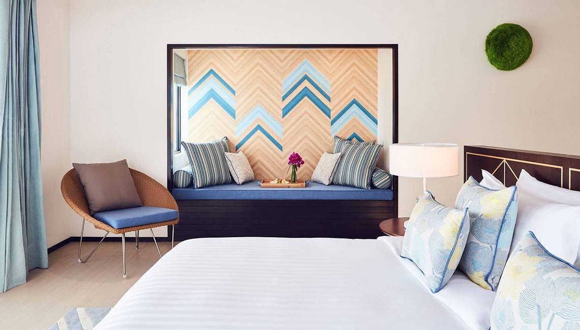Hotelzimmer im Amari Havodda Maldives mit Bett, Sitzbank, Kissen und Lampe.