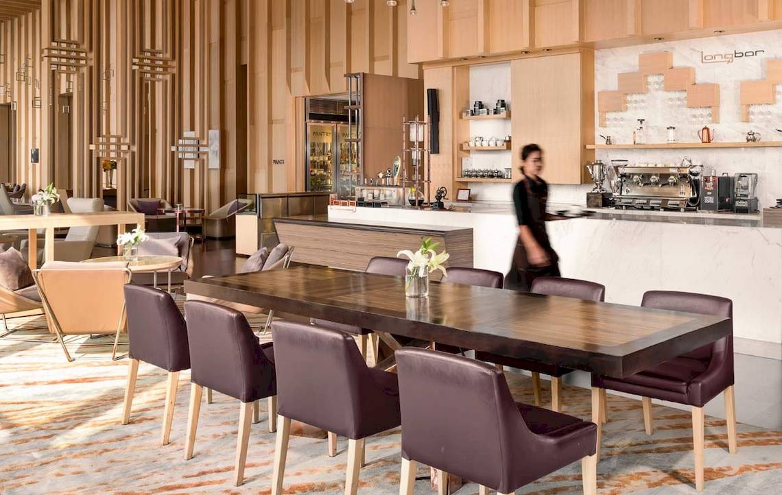AVANI+ Riverside Bangkok Hotel Innenraum mit Esstisch, Stühlen und Bar.