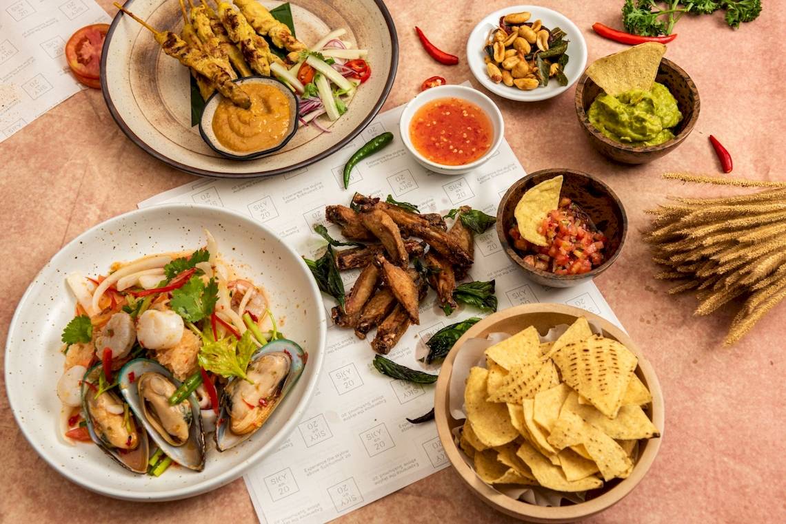 Essen und Beilagen von Novotel Bangkok Sukhumvit 20, einschließlich Salat, Dips, Tortilla-Chips und Getränke.