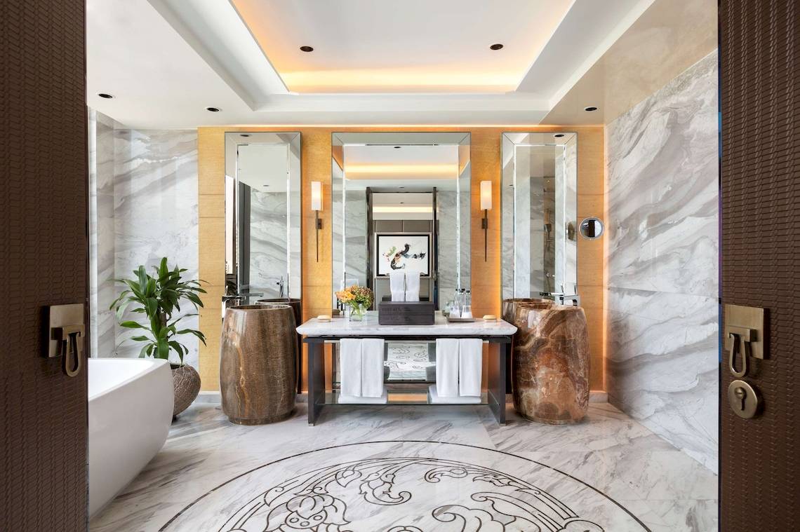 Innenansicht des Badezimmers im Siam Kempinski Hotel Bangkok mit Marmorwänden und einem zentralen Waschtisch.
