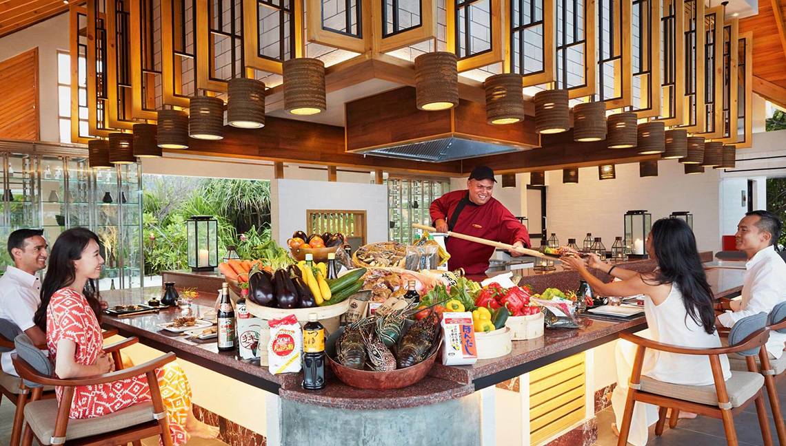 Menschen sitzen an einem Buffettisch im Amari Havodda Maldives Hotel und essen mit einem Koch.