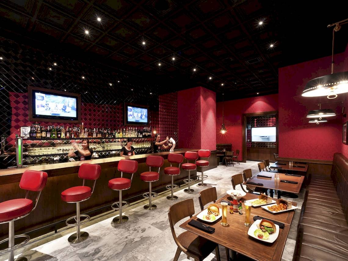 Innenbereich des Pullman Bangkok Hotel G mit roter Bar, Sitzstühlen und Essenstischen.