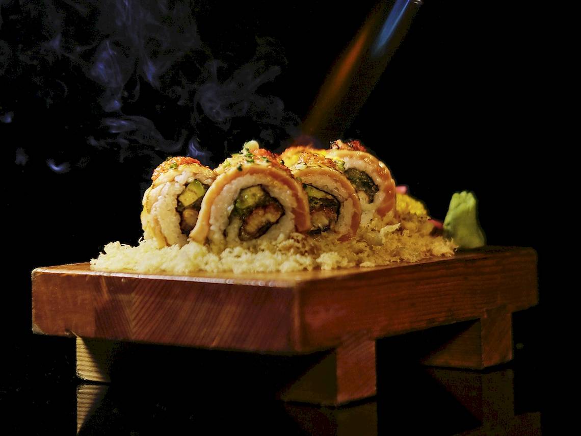 Sushi mit Raucheffekt auf einer Holzplatte serviert, mit Reis und Gemüse gefüllt