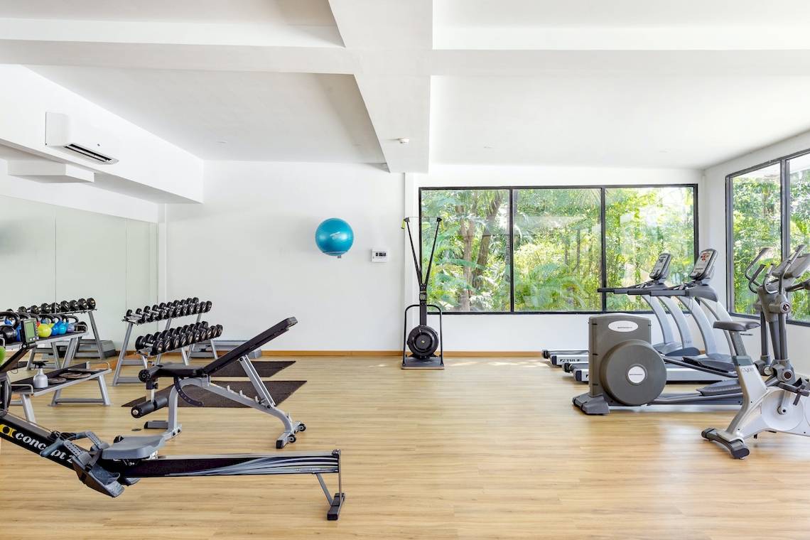 Fitnessstudio im Sunprime Kamala Beach mit verschiedenen Geräten und großen Fenstern.
