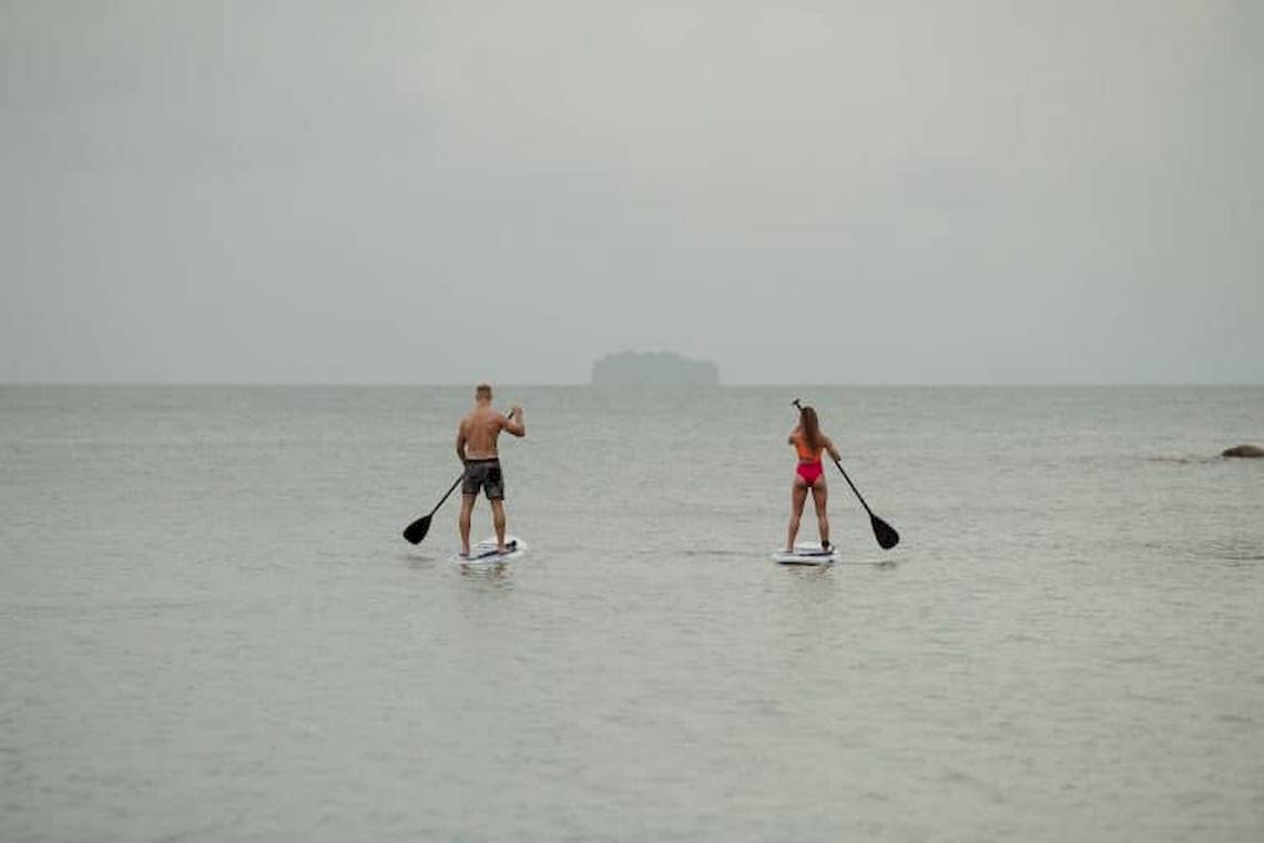 Zwei Paddler im Meer, einer in Badehose und die andere in Bikini, beide auf Paddelbrettern.