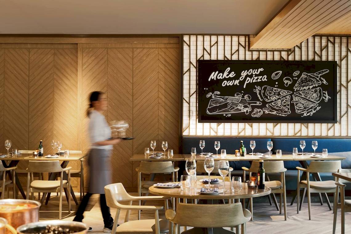 Restaurant-Innenansicht im Phuket Marriott Resort & Spa Merlin Beach mit einer Tafel, auf der 'Mach deine eigene Pizza' steht.