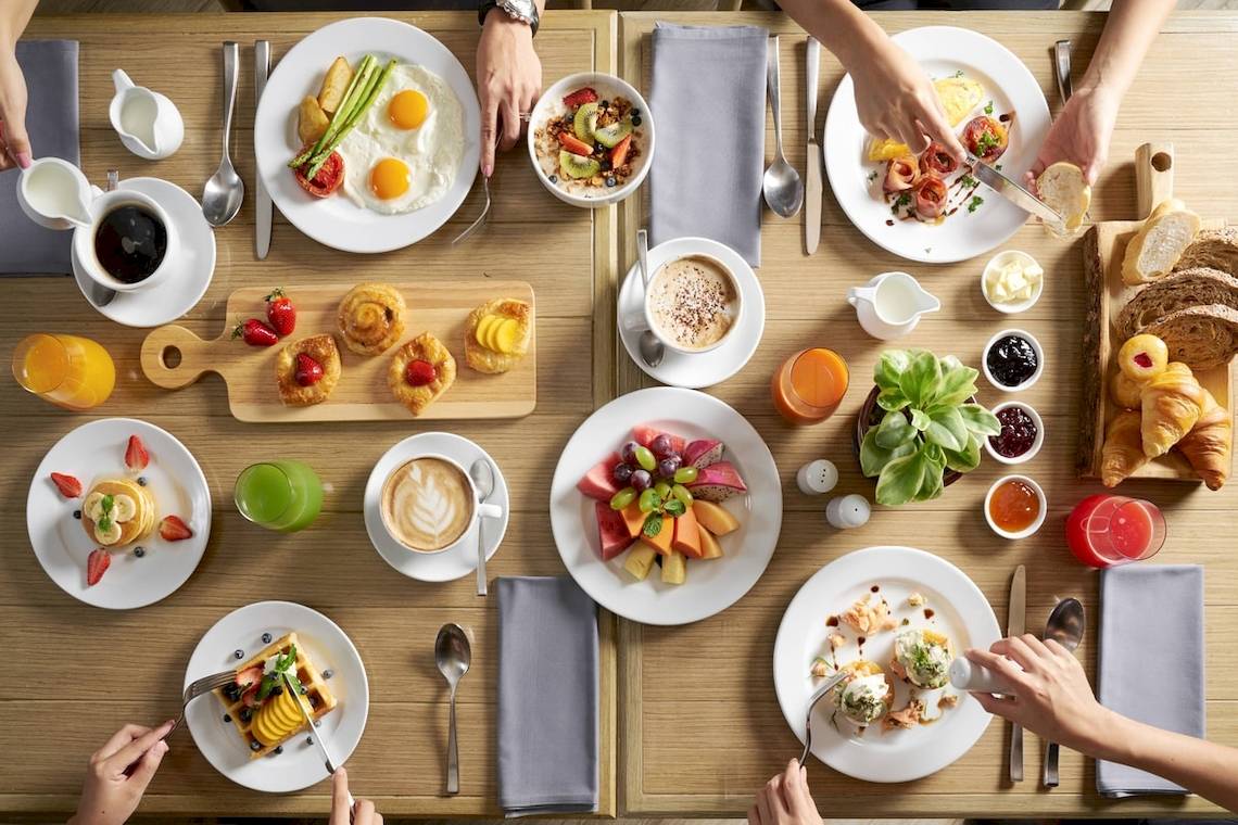 Frühstückstisch im Phuket Marriott Resort & Spa Merlin Beach mit verschiedenen Gerichten, Früchten und Getränken.