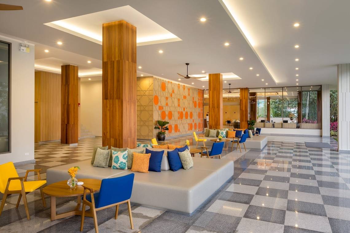 Lobby des X10 Khaolak Resorts mit gemusterten Bodenfliesen, Holzsäulen und bunten Kissen auf der Bank.