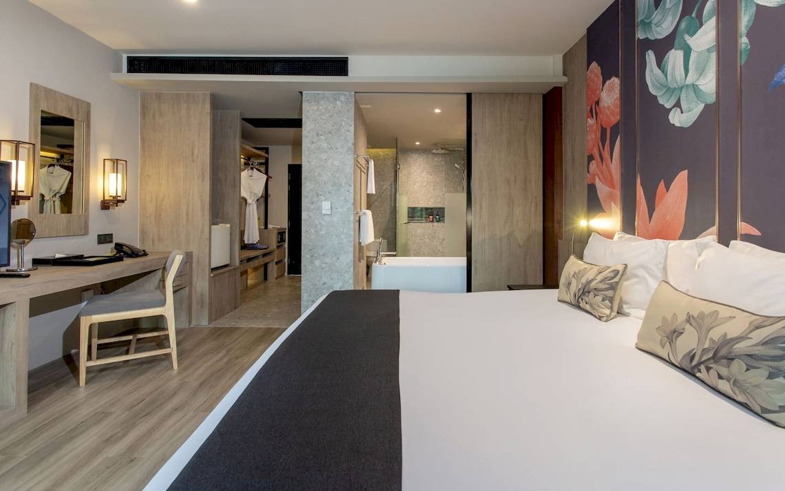 Innenansicht eines Hotelzimmers im La Flora Khao Lak, mit einem Bett, Schreibtisch und Badezimmer.