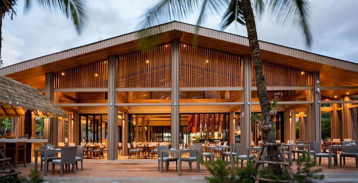 Außenbereich des La Flora Khao Lak Hotels mit modernen Holzarchitekturen, Tischen und Stühlen.