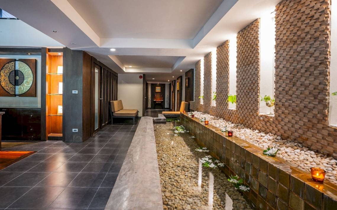 Eingangsbereich des La Flora Khao Lak Hotels mit Wasserlauf und Steinmauer.