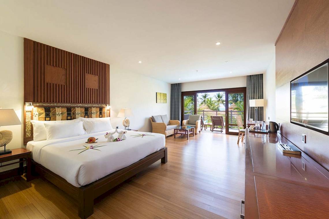 Innenansicht eines Hotelzimmers im The Haven Khao Lak mit Bett, Wohnzimmer und Terrasse.