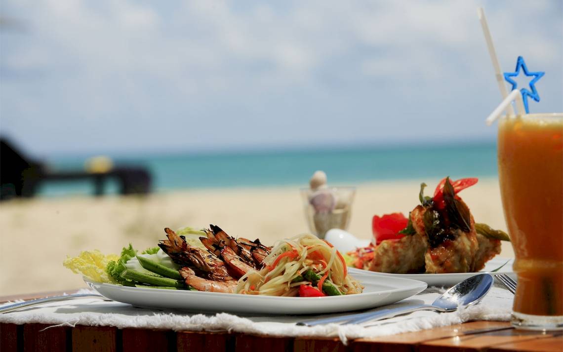 Tisch am Strand mit Essen und Getraenke, Hintergrund zeigt Meer und Himmel