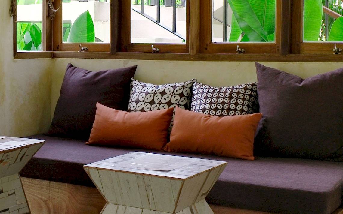 Sofa vor Fenster im Bangsak Village mit braunen und orangefarbenen Kissen.
