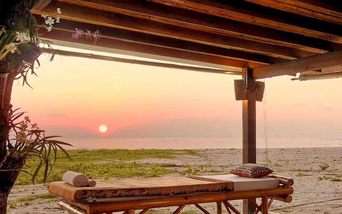 Zwei Massagebetten auf dem Strand unter einem Dach während des Sonnenuntergangs.