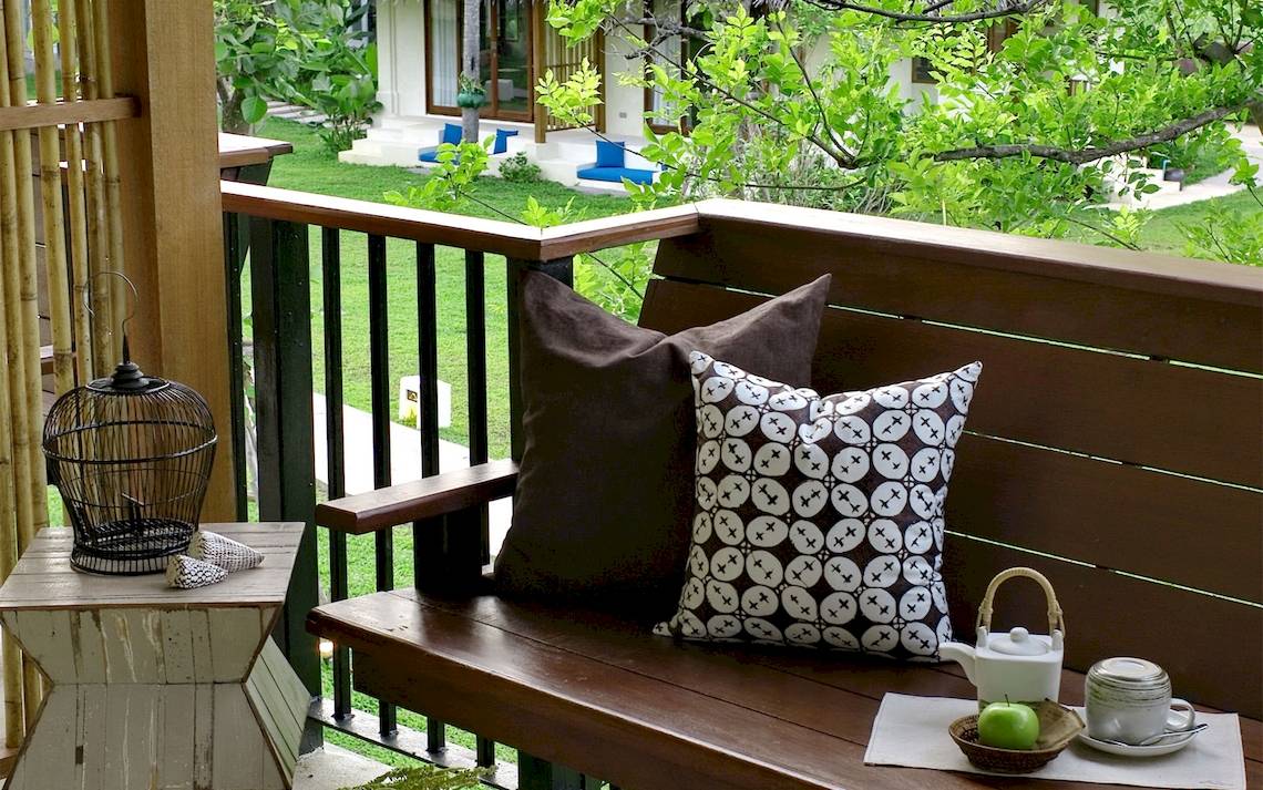 Ein Sofa auf einer Terrasse mit grünem Hintergrund und einem Tisch mit Dekor.